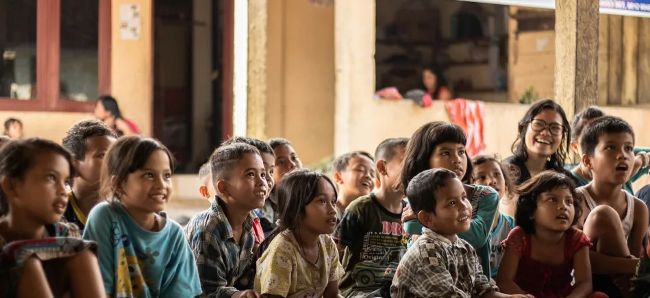 Anak-anak duduk bersama di lantai ruang komunitas, tersenyum sambil menyimak paparan.