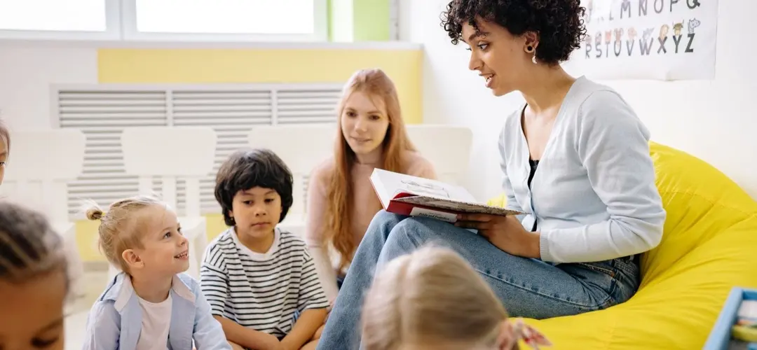 Fasilitator membacakan buku kepada anak-anak di ruang belajar yang terang.